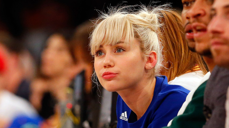 Blond Miley Cyrus watching a sporting event