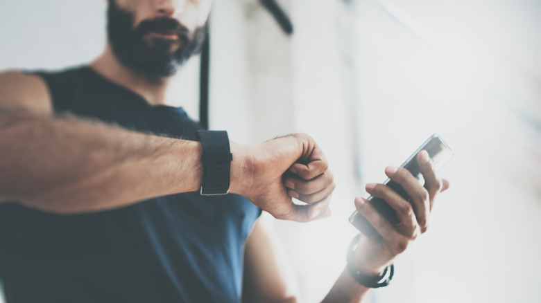 Man checks fitness tracker and phone