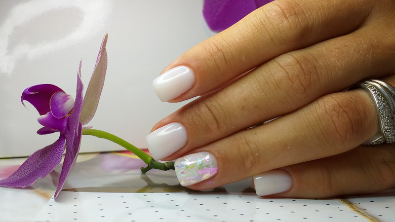 Hand with white nails holding purple flower