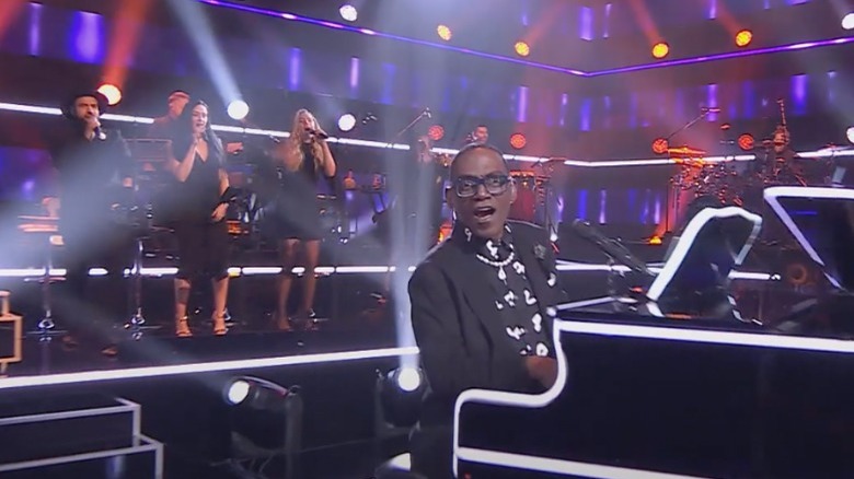 Randy Jackson playing the piano in front of the live band on Name That Tune