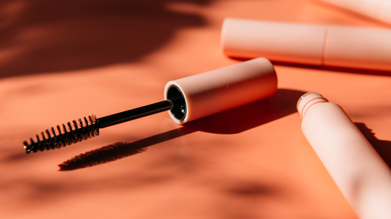 An open tube of mascara on a coral background. 