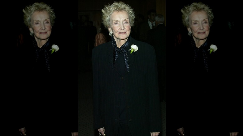 Nina Foch posing in black coat with white rose pinned to her lapel