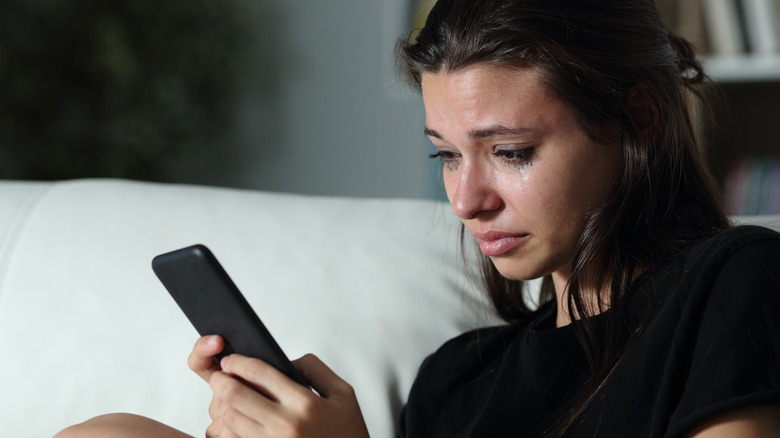 Woman crying while looking at her phone