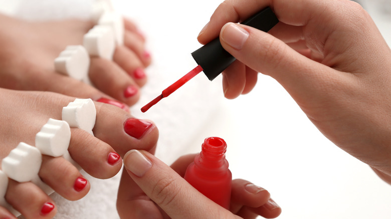 manicurist painting red on client's toe nails