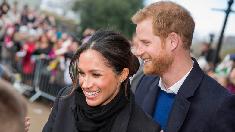 prince harry and meghan markle smiling with a crowd of people