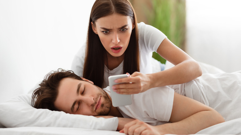 Woman checking sleeping man's phone