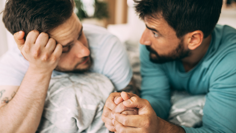 Men holding hands on bed