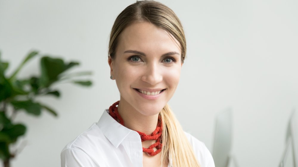 Woman smiling in a white business outfit with a bold accessory