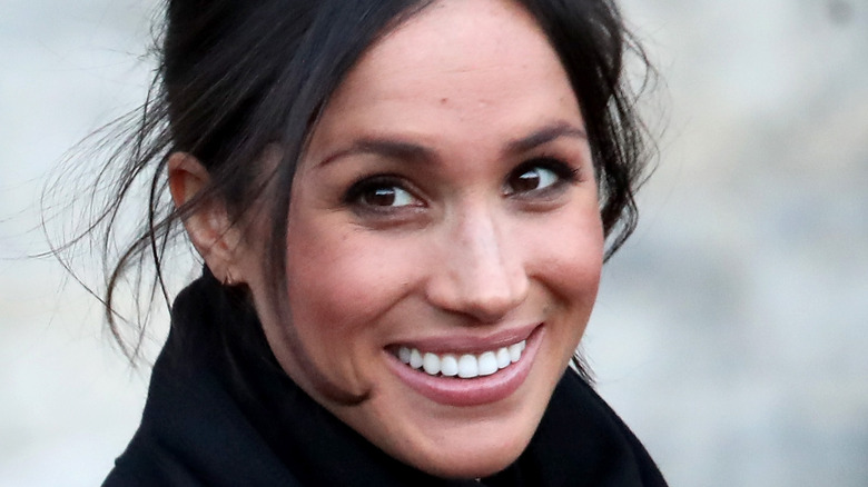 Meghan Markle smiling in black with her hair up