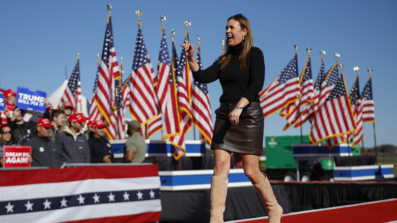 Sarah Huckabee Sanders attends a Trump event wearing a leather skirt, a black turtleneck, and tall tan boots