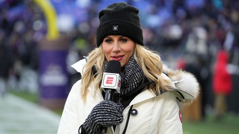 Laura Rutledge in coat, hat, scarf, and mittens speaking into mic on football field