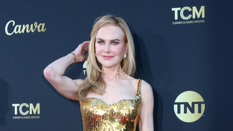 Nicole Kidman smiling with hand to her hair in shiny gold dress