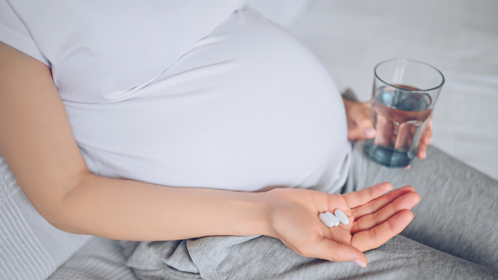 Pregnant woman holding pills and a glass of water 