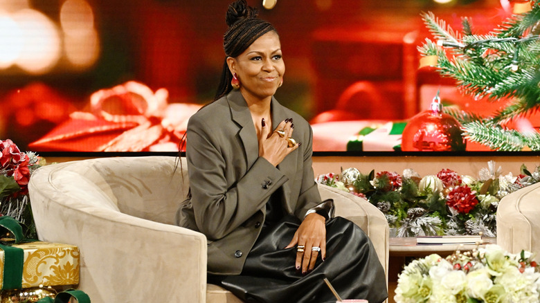 Michelle Obama seated in an olive suit with her hand over her heart