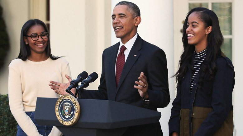 Barack Obama speaking with Sash and Malia smiling and standing beside him