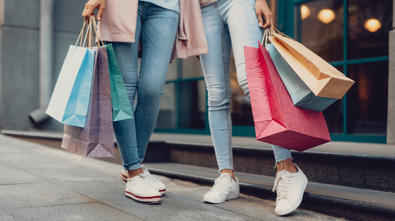 Two people wearing jeans carrying shopping bags 