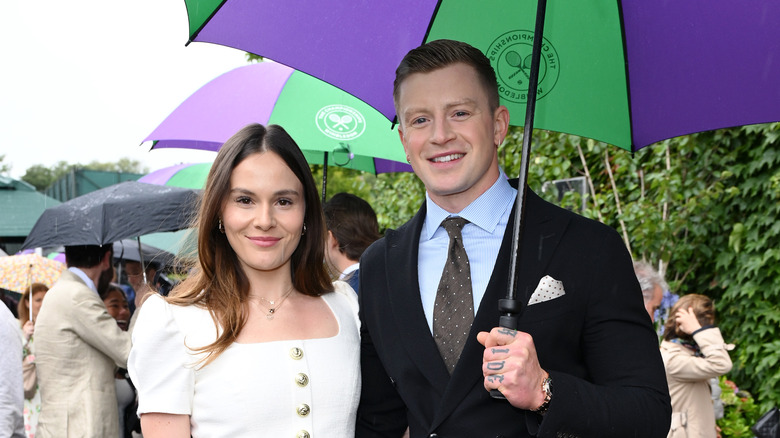 Holly Ramsay and Adam Peaty standing under an umbrella at an event