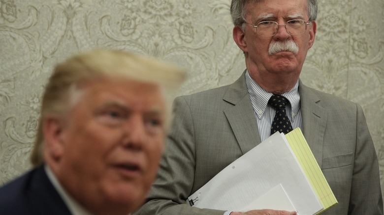 John Bolton staring at an out of focus Donald Trump