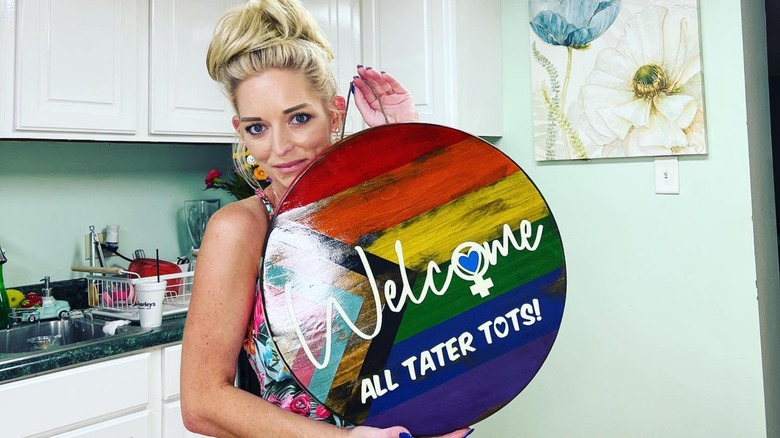 Ophelia Nichols holding a rainbow Welcome All Tater Tots sign