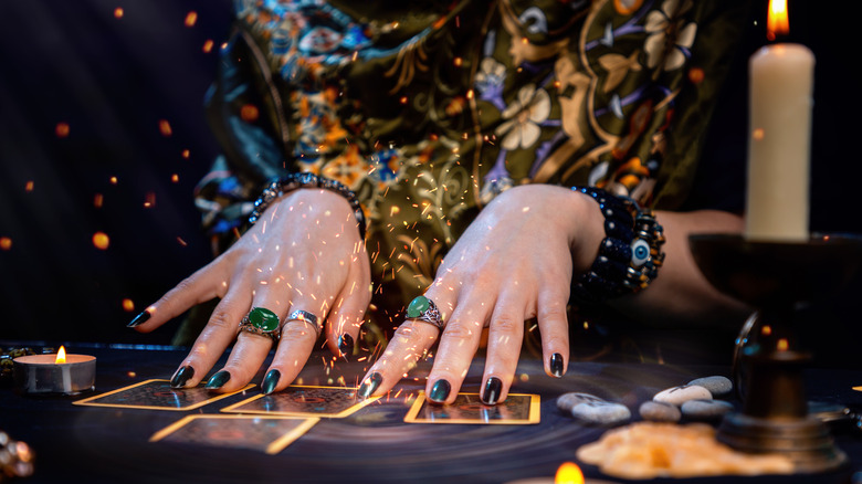 A woman's hands placed on a table with cards and candles