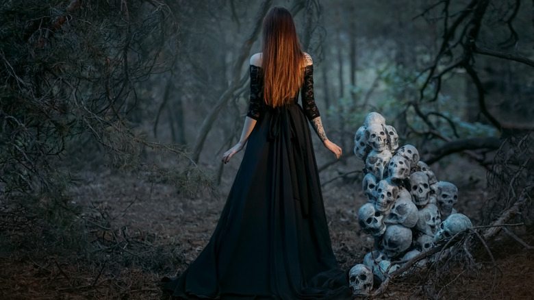 Woman in black dress standing in the middle of the woods with her back to the camera