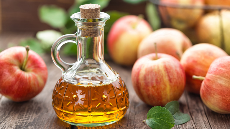 A jug of apple cider vinegar surrounded by apples