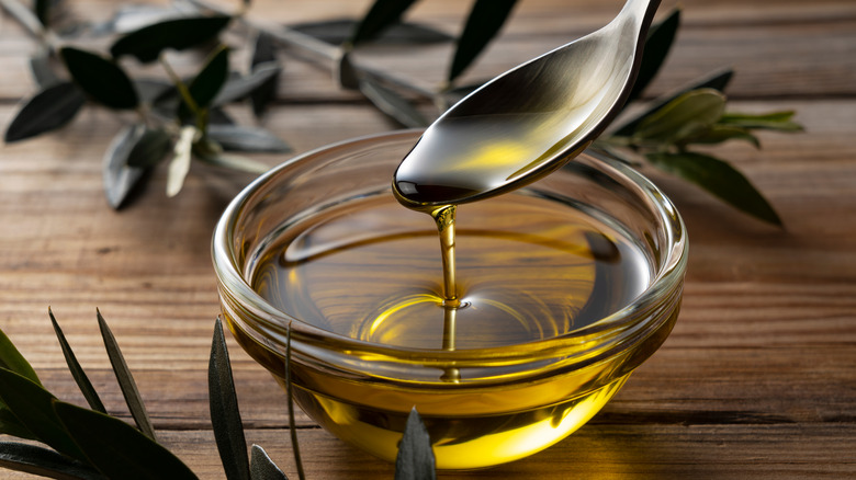 A metal spoon scooping up olive oil out of a glass bowl