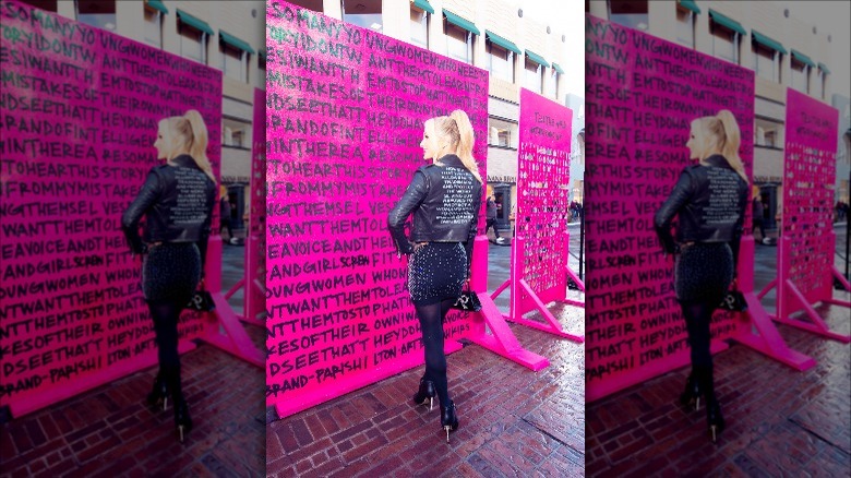 Paris Hilton posing by display panel advocating #THISISWHOIAM campaign