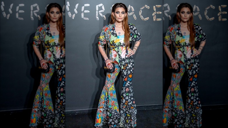 Paris Jackson posing on step-and-repeat in colorful Versace pantsuit