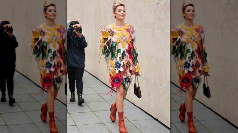 Paris Jackson walking while holding up peace sign and being photographed by paparazzi behind her