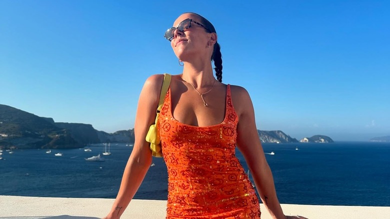 Pauline Ducruet stands outside in front of the sea in an orange dress with her face in the sun.