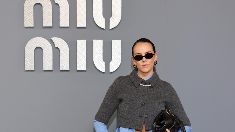 Pauline Ducruet wears sunglasses and pearls in front of Miu Miu's logo.