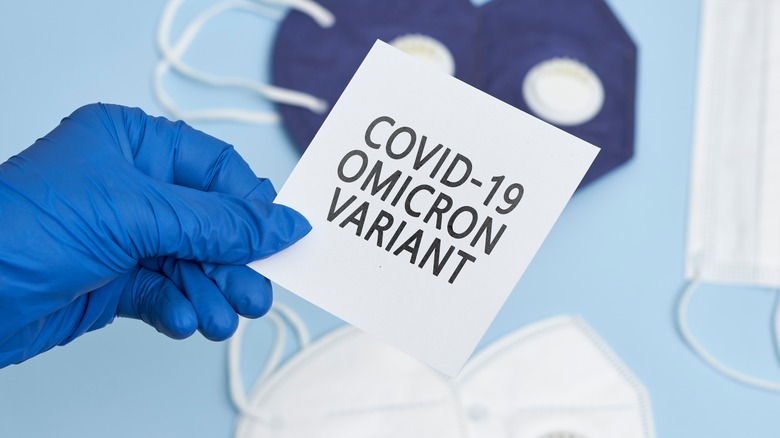 Masked hand holding paper that says "COVID-19 OMICRON VARIANT"