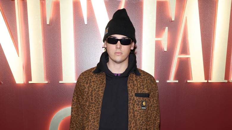 Paris Brosnan wears sunglasses and a beanie posing at a Vanity Fair event.