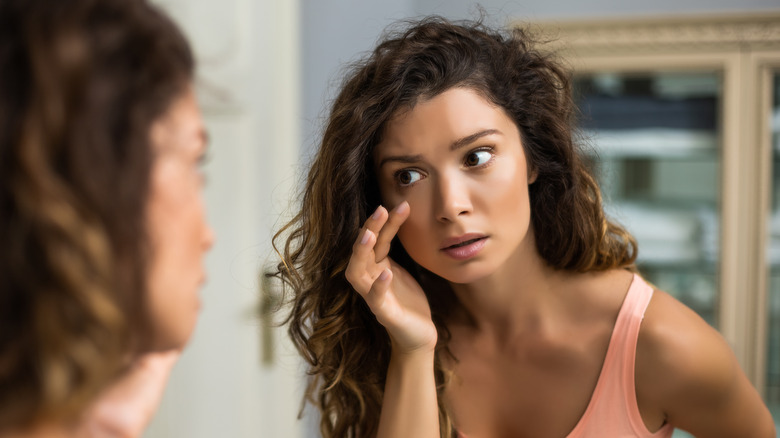 woman examining skin in bathroom mirror