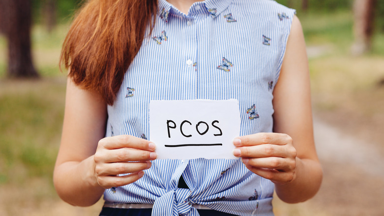 woman holding a paper with PCOS on it