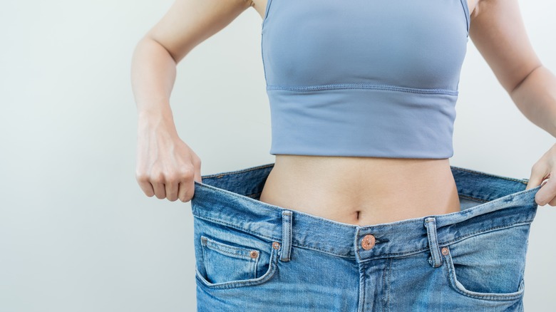 woman showing her weight loss with big jeans