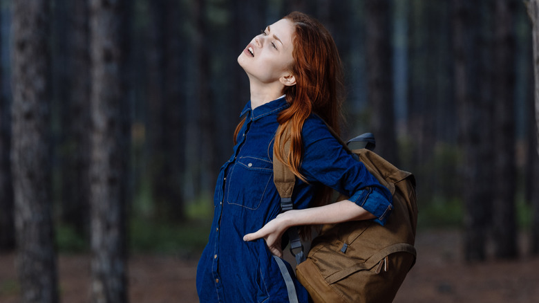 A woman standing in the woods with a heavy backpack, a posture mistake