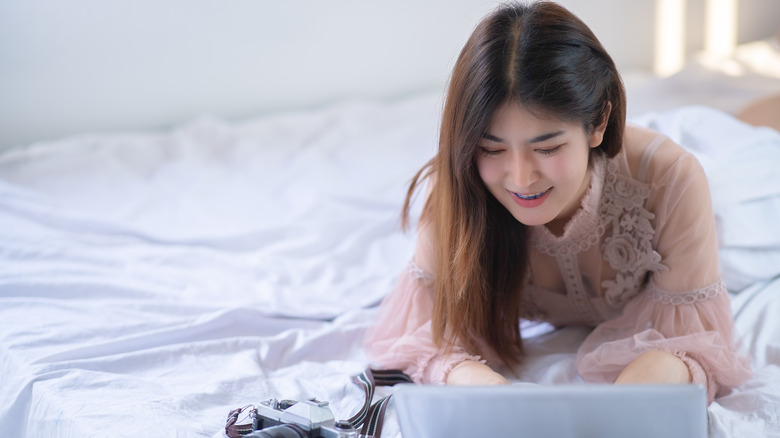 A woman hunched over her laptop in bed, a posture mistake