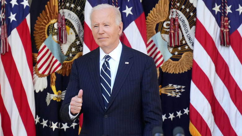 Joe Biden giving thumbs up in front of several flags