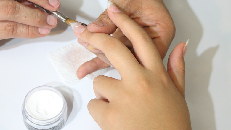 Hand applying acrylic powder on nail