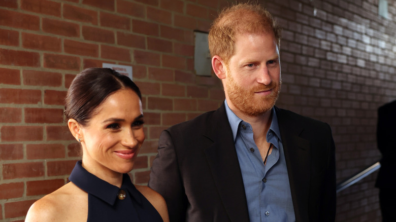 Meghan Markle smiling while Prince Harry looks thoughtful