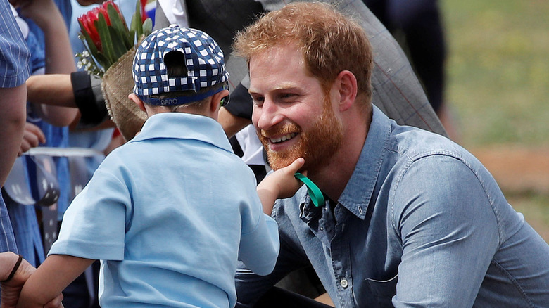 Prince Harry smiling as a little boy touches his beard