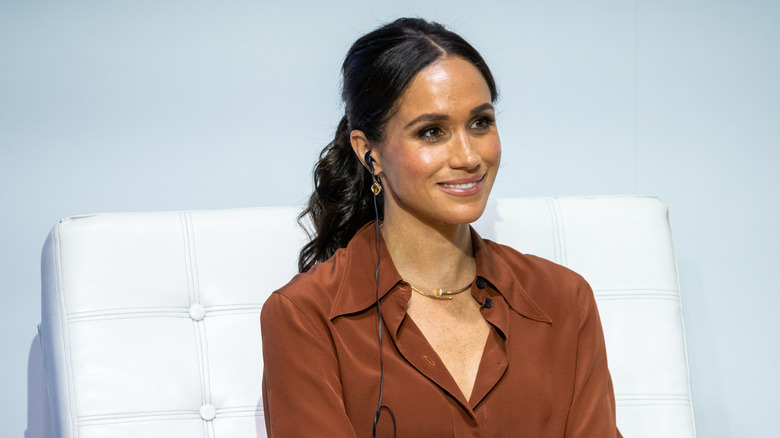 Meghan Markle smiling in white chair at an event