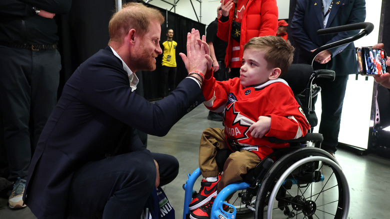 Prince Harry high fives a child in a wheelchair.