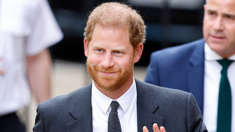 Prince Harry smiling and waving with security behind him