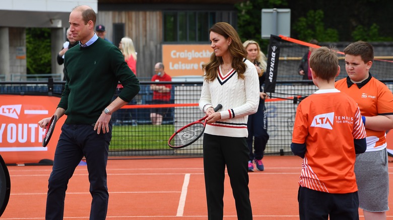 Prince William and Princess Catherine on the tennis court holding racquets