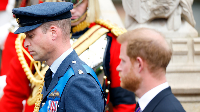 Prince William bows his head while standing next to Prince Harry