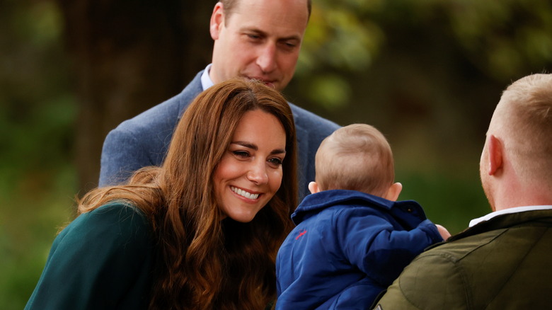 Kate Middleton smiling at a baby as Prince William stands beside her