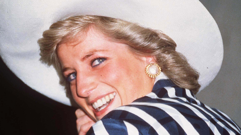 Princess Diana smiling, holding a large hat 